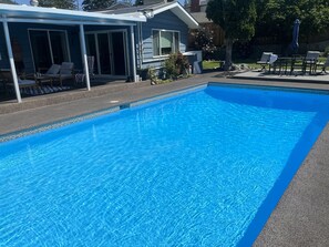 Una piscina azul cristalina con un porche cubierto y mobiliario de exterior.