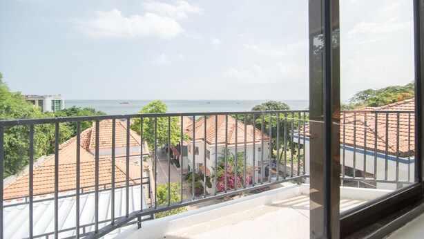 A balcony with a metal railing overlooking a residential area with red-tiled roofs and a view of the sea. - RedDoorz Plus near Bai Truoc (Ho Chi Minh City)