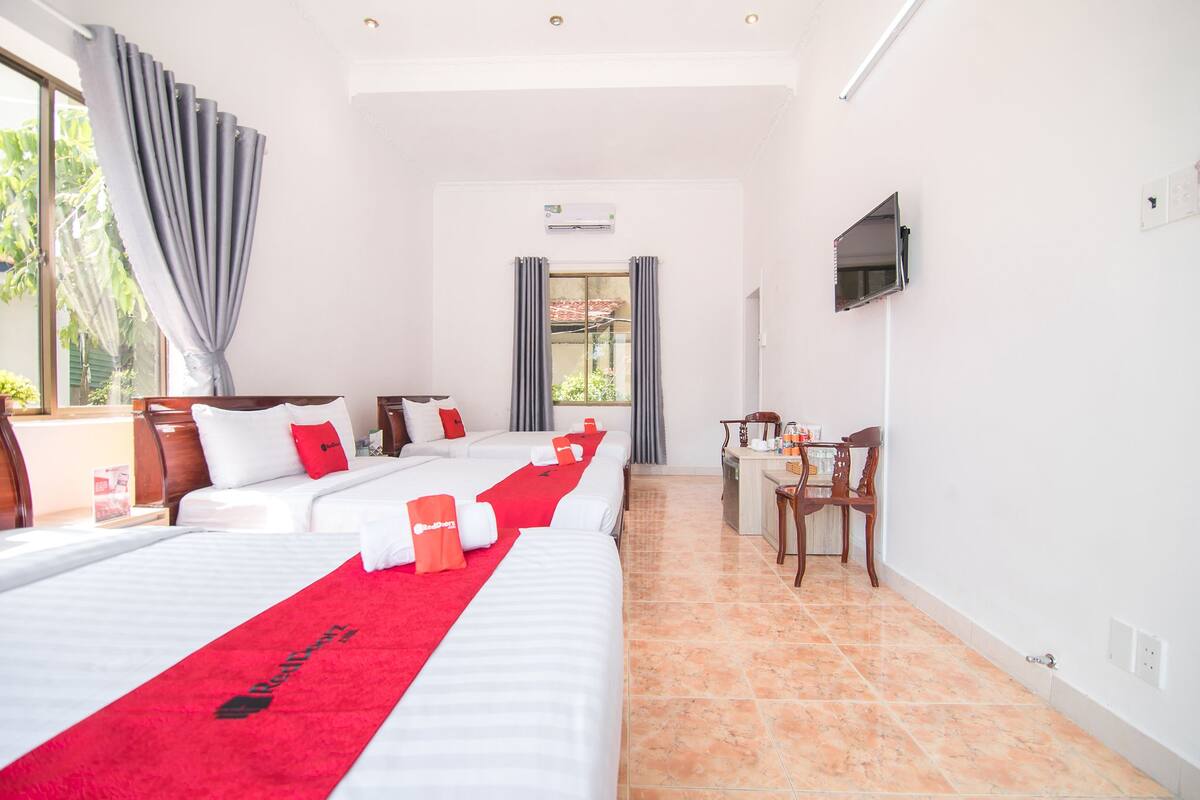 Habitación de hotel con dos camas, un escritorio, una silla, un televisor y una ventana con cortinas.
