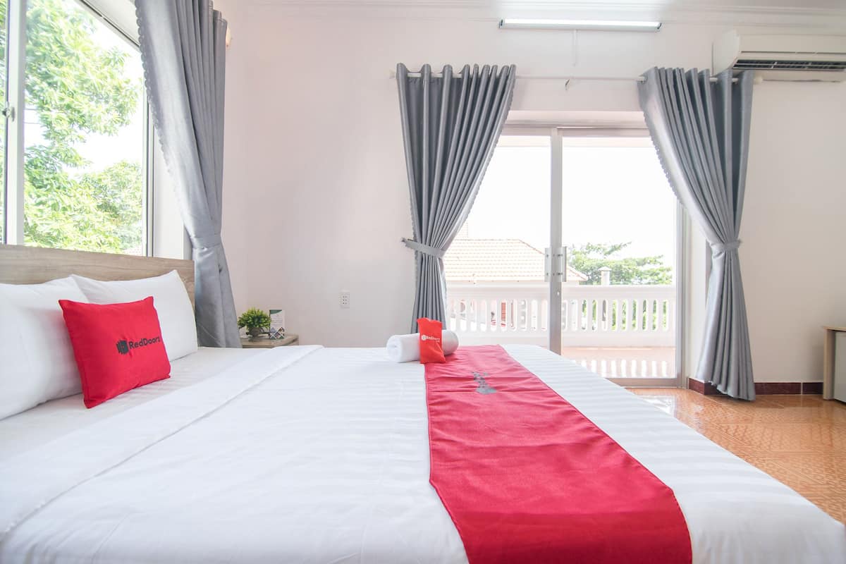 Una habitación de hotel con una cama, una almohada roja, una toalla roja y un balcón con cortinas.
