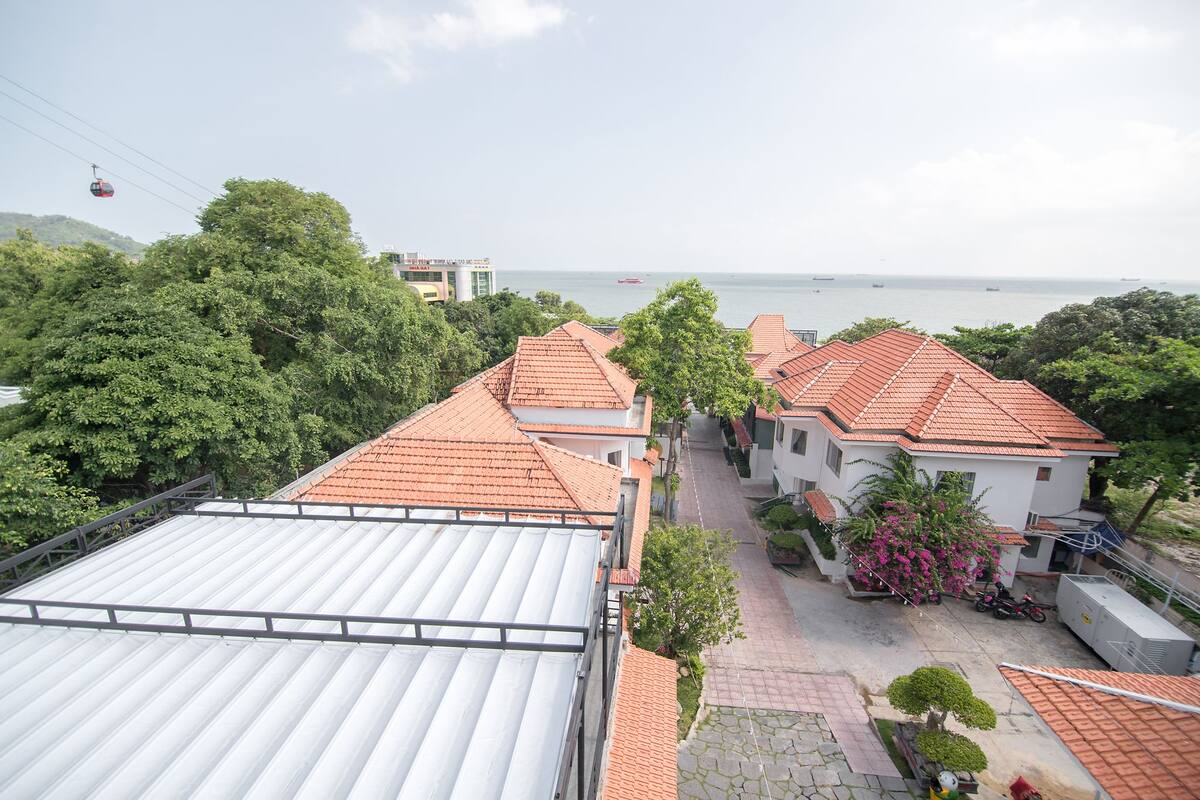 Un barrio residencial con tejados de tejas rojas, un sendero pavimentado y vista al mar.