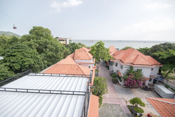 A residential area with red-tiled roofs, a paved pathway, and a view of the sea.