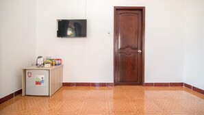 A room with a patterned floor, a wooden door, a small refrigerator with a plant and snacks, and a flat-screen TV mounted on the wall. - RedDoorz Plus near Bai Truoc (Ho Chi Minh City)