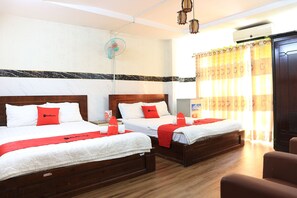 A hotel room with two beds, each with white bedding and red accents, a wooden floor, a ceiling fan, and a window with curtains.