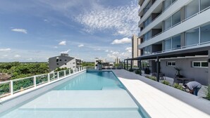 Una piscina al terrat amb una vista clara del paisatge urbà, envoltada d'edificis moderns i vegetació.