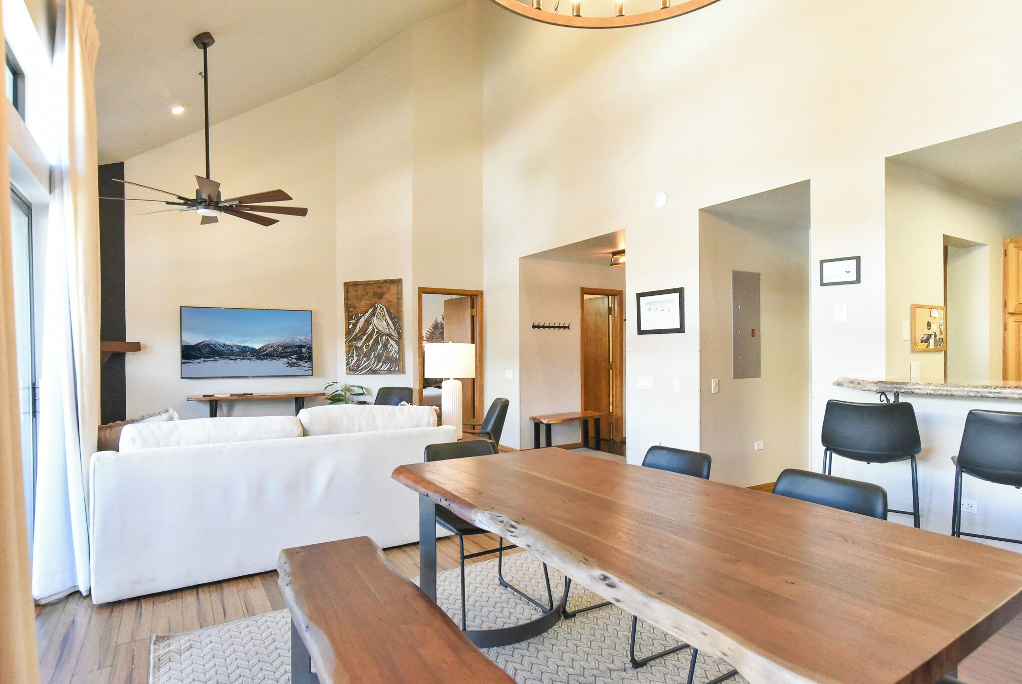 A modern living room with a wooden dining table, white sofa, and a ceiling fan.