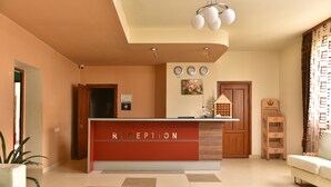 Uma área de recepção com balcão vermelho, um relógio e um quadro na parede.