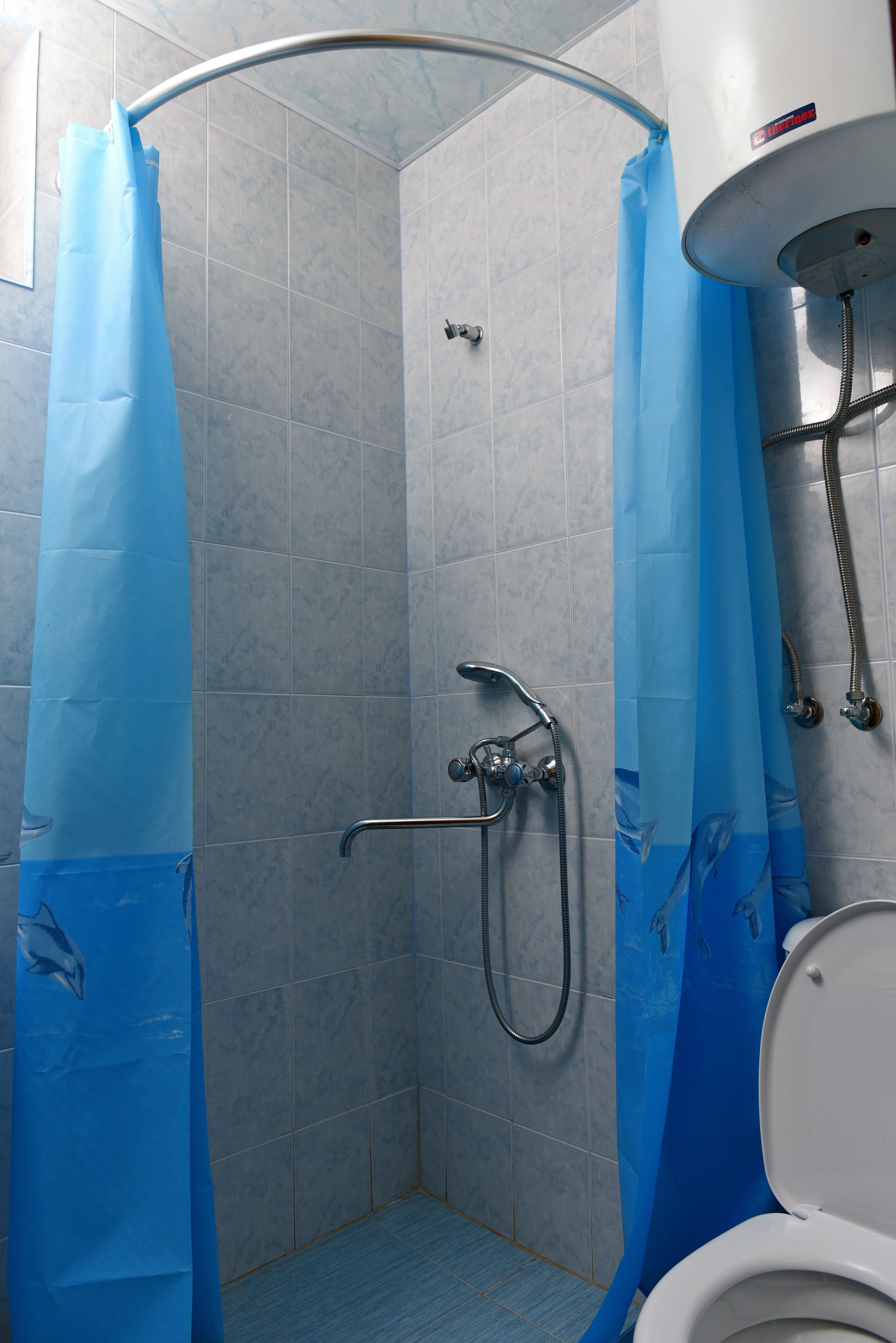 Un box de ducha con cortina azul, un cabezal de ducha de mano y una manguera de ducha.