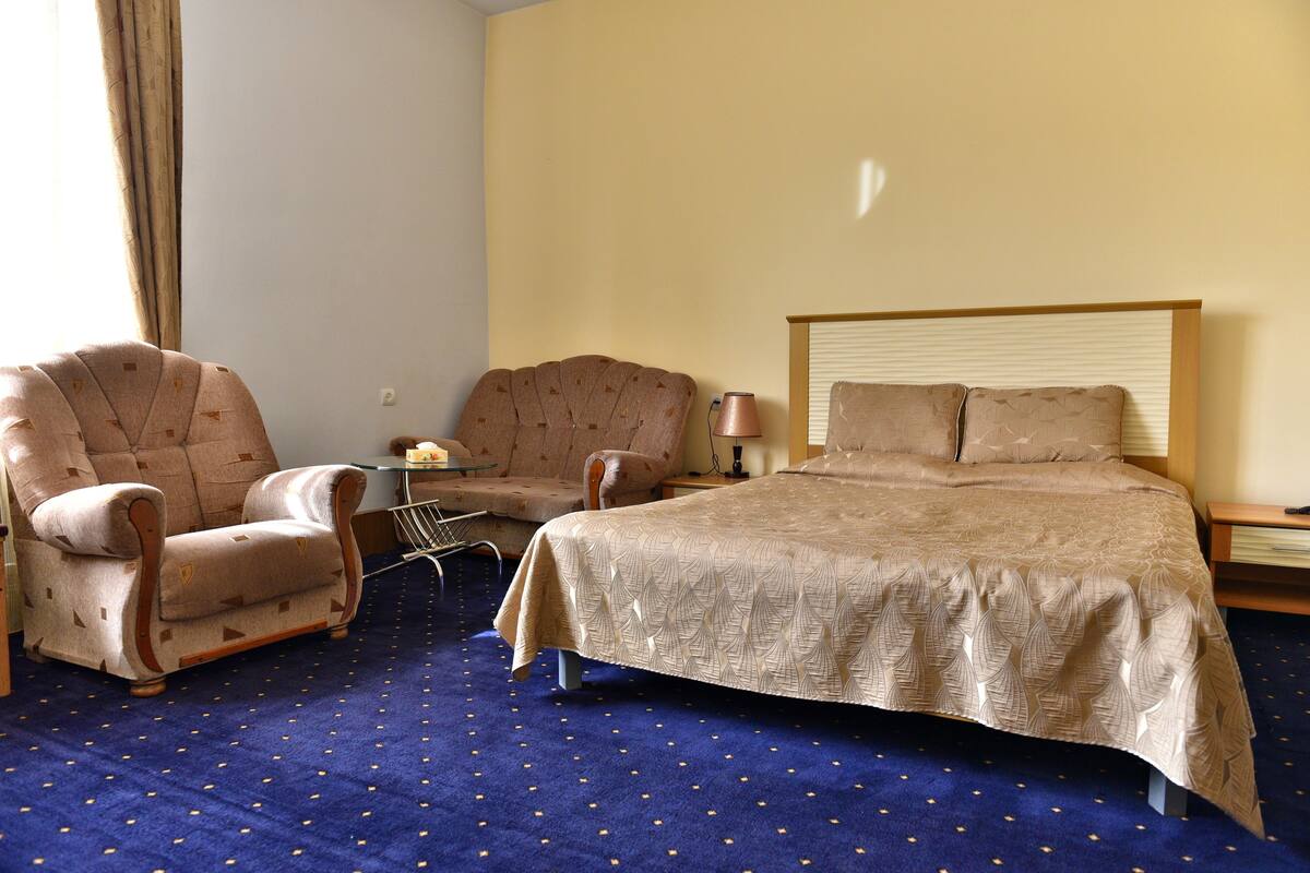 A hotel room with a large bed, two armchairs, a small table, and a lamp.