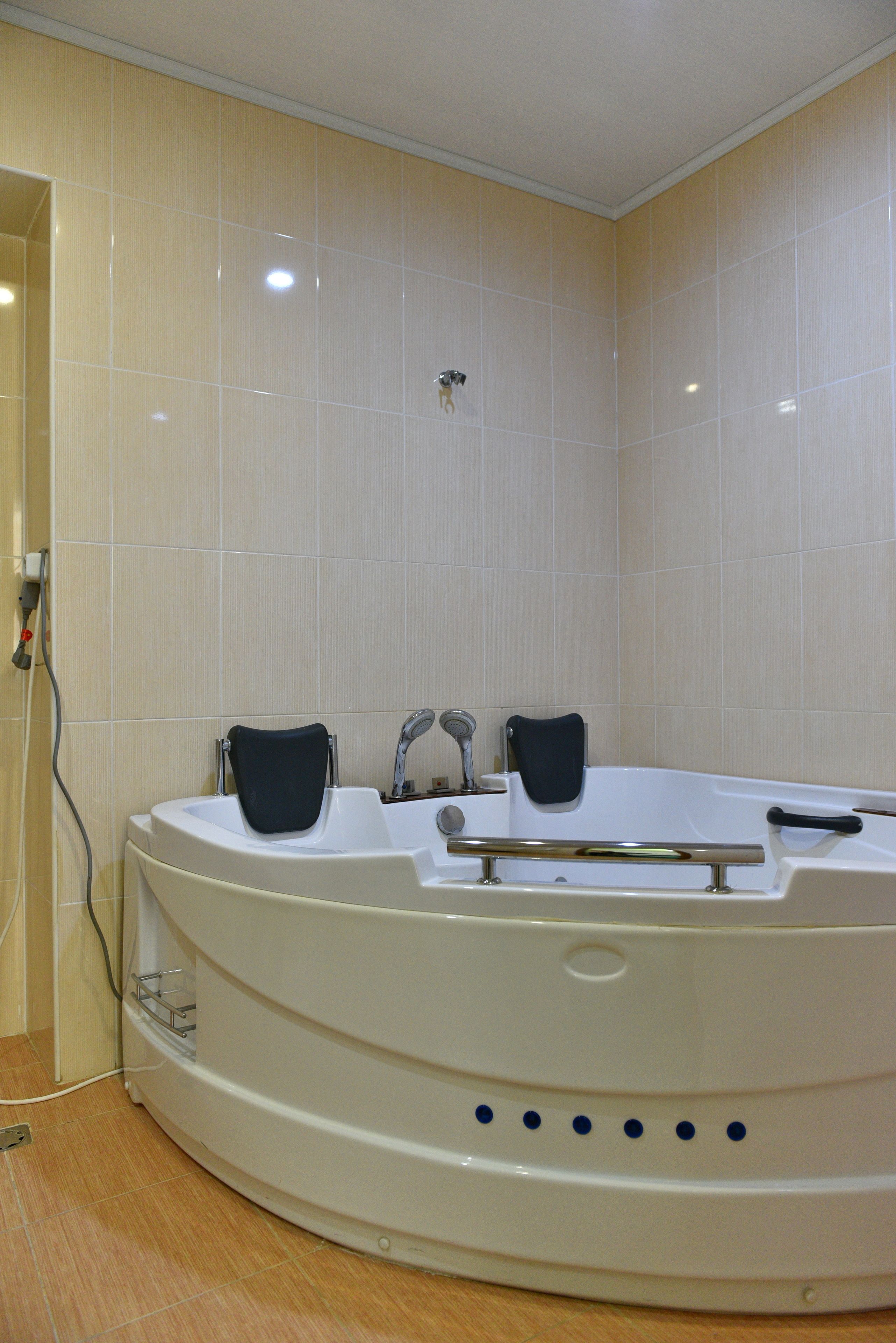 A modern bathroom with a large bathtub, two black bath seats, and a handheld showerhead.
