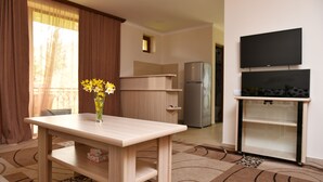 Uma sala de estar moderna com uma mesa de madeira, um vaso com flores, uma televisão de tela plana e uma área de cozinha ao fundo.