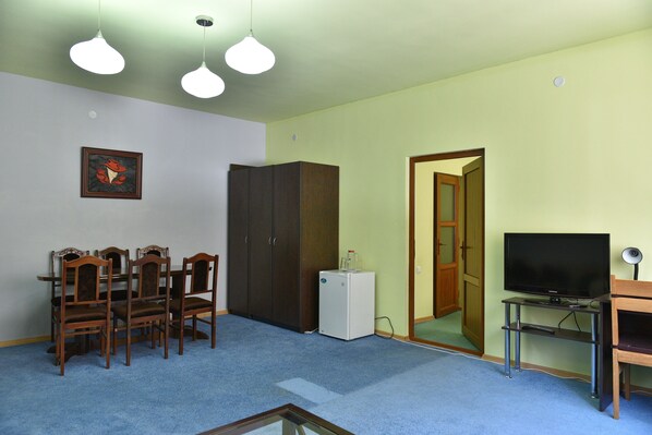 Una habitación con una mesa de comedor y sillas, un televisor, un refrigerador pequeño y un armario.