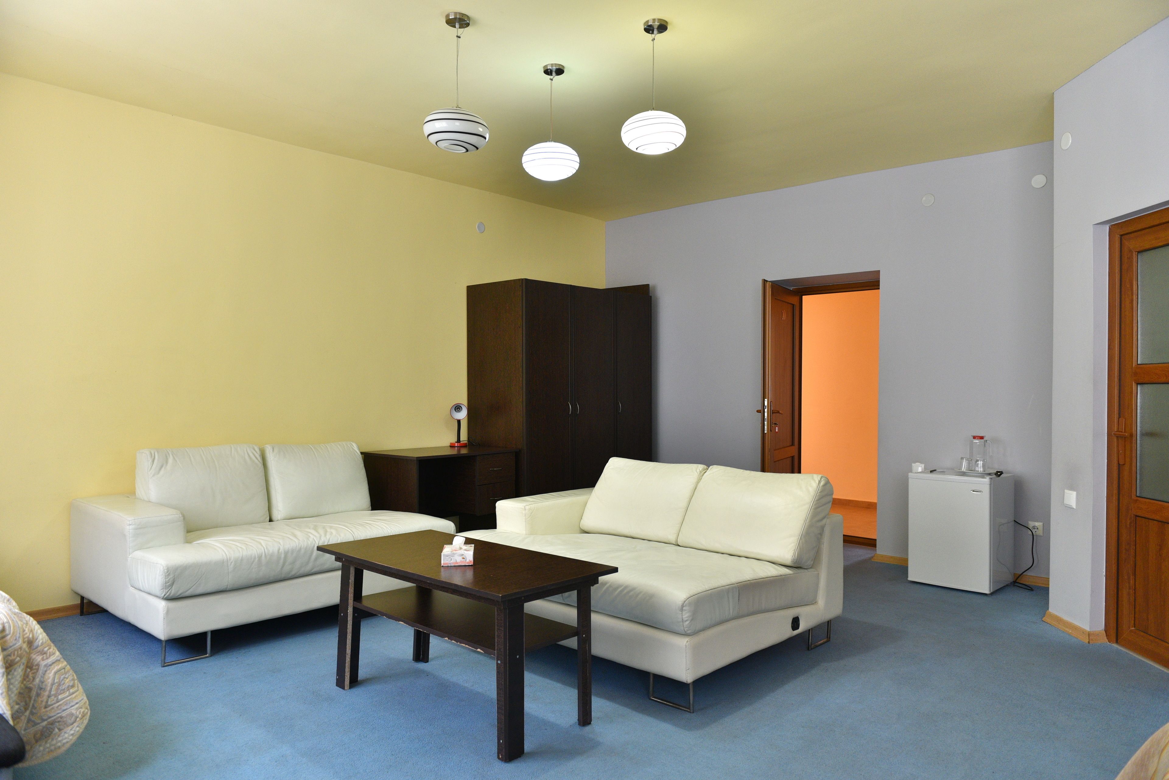 A living room with two white sofas, a wooden coffee table, and a small white refrigerator.