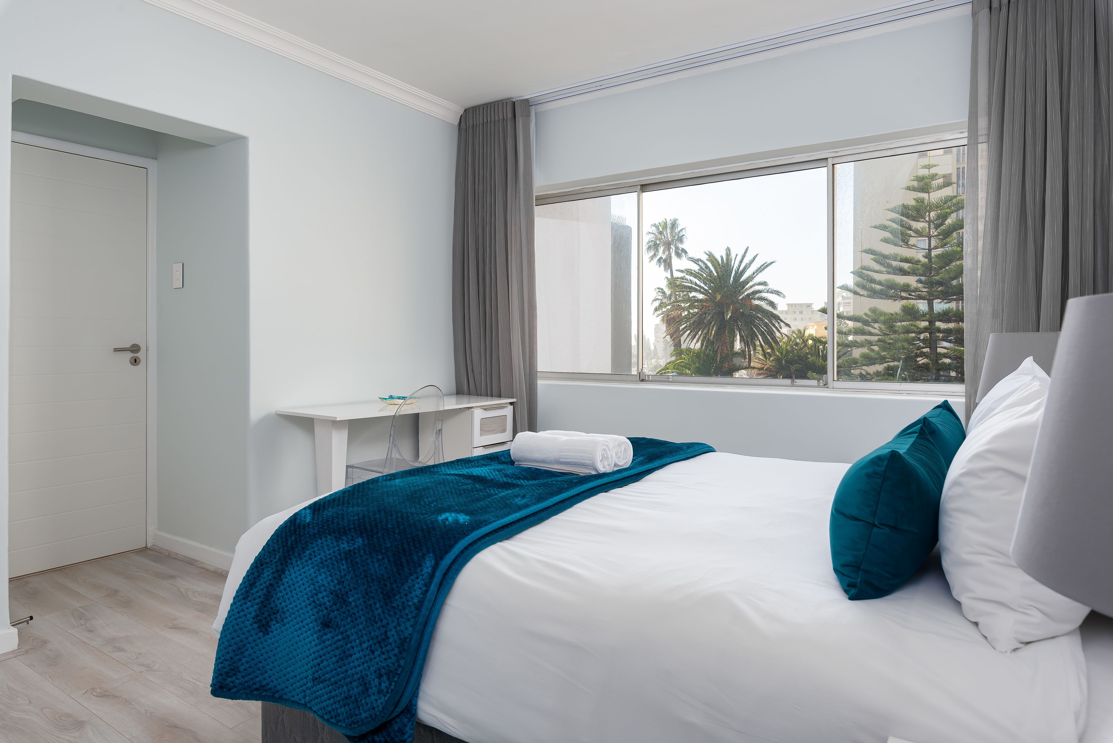 A hotel room with a bed, a desk, and a window with a view of palm trees.