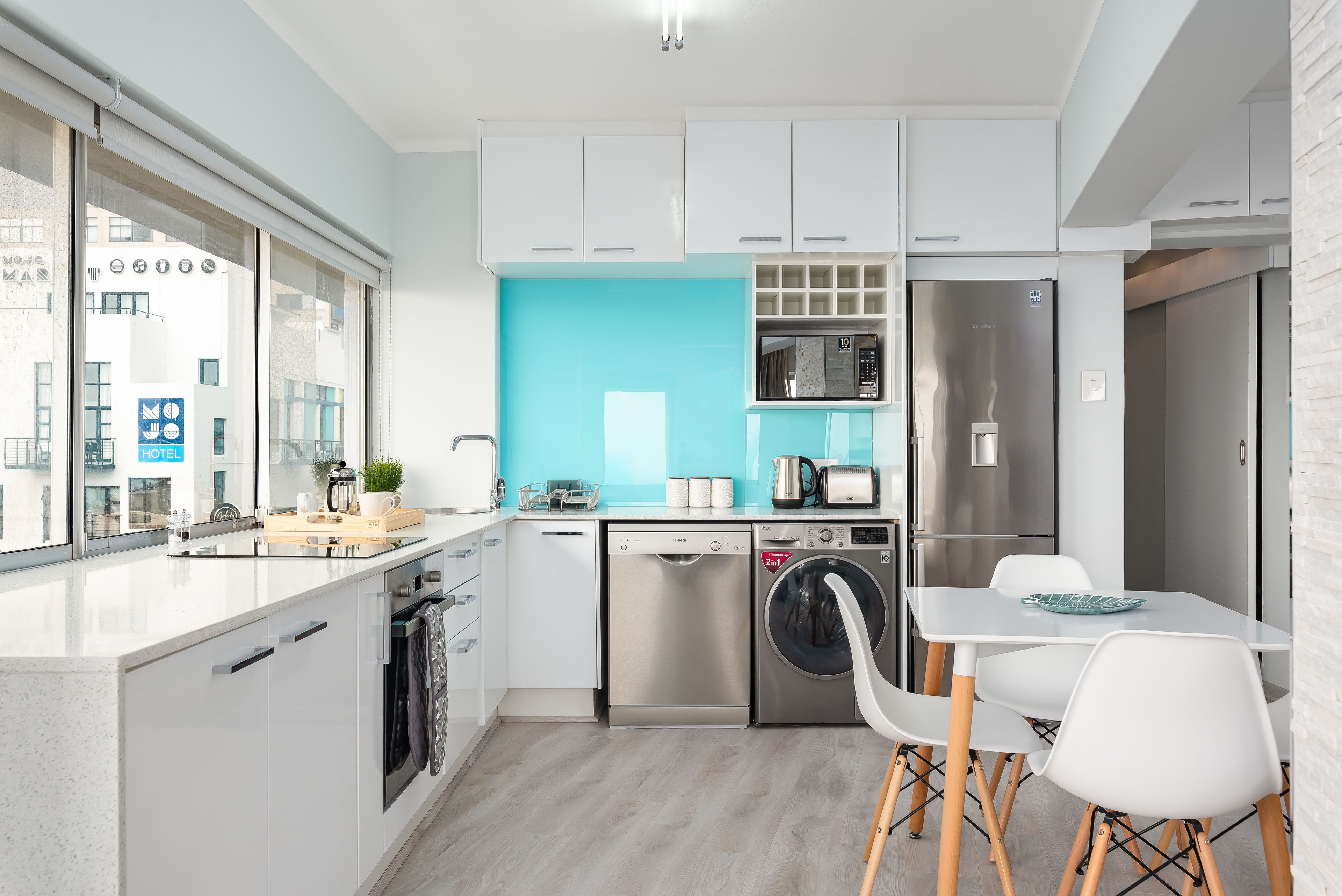 Una cocina moderna con armarios blancos, lavavajillas, lavadora, microondas y refrigerador de acero inoxidable.