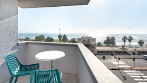 A balcony with a table and chairs, overlooking a coastal area with palm trees and a building in the background. - Saratoga 304 (Cape Town)