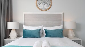 A neatly made bed with white and teal bedding, two teal pillows, and a pair of rolled white towels on a teal throw. - Saratoga 304 (Cape Town)