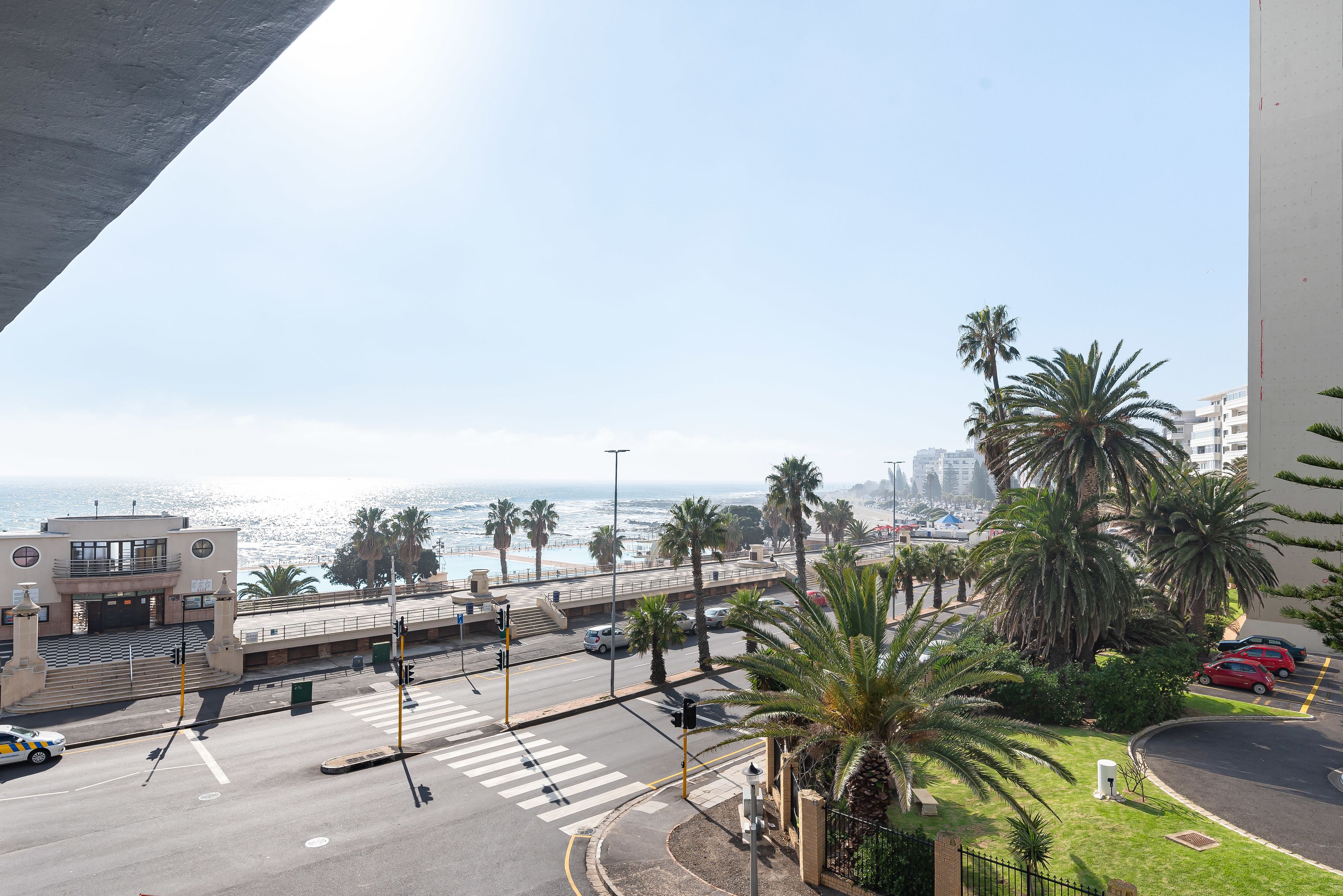 Une intersection située sur la côte, bordée de palmiers, avec un passage piéton et une vue sur l’océan.