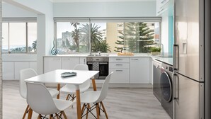 A modern kitchen with a dining area, large windows, and a view of palm trees and buildings. - Saratoga 304 (Cape Town)