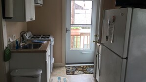 Une cuisine compacte équipée d’une cuisinière, d’un évier et d’un réfrigérateur. Une porte donne accès à un balcon avec vue sur l’extérieur.