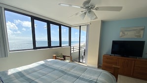 A bedroom with a large bed, a ceiling fan, a TV, and a view of the ocean through large windows. - OCEANFRONT NEAR THE PIER!OCEAN VIEW FROM EVERY ROOM! 2-2 WRAPAROUND BALCONY! (Daytona Beach)