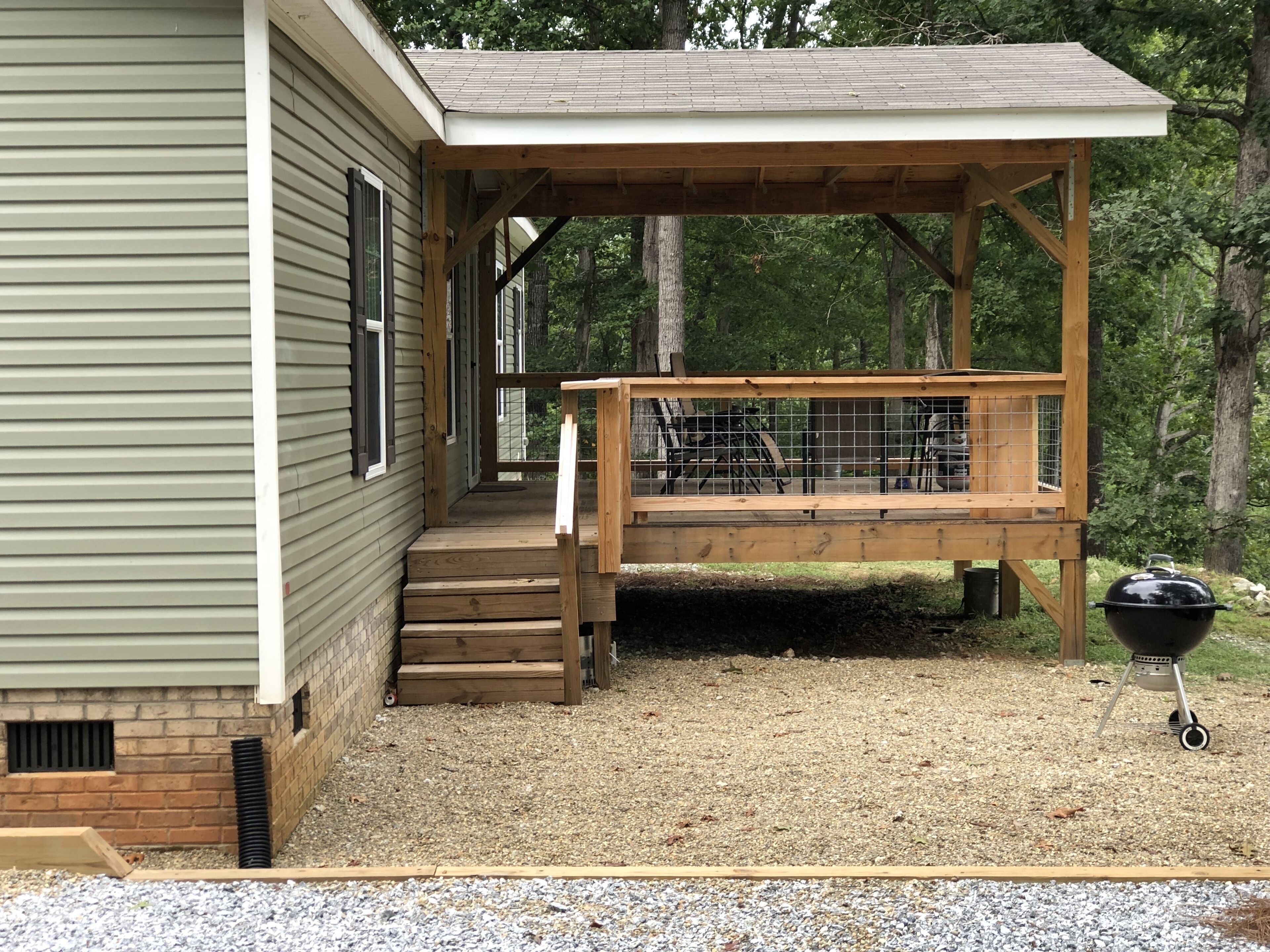 A wooden deck attached to a house with a covered porch and a barbecue grill.