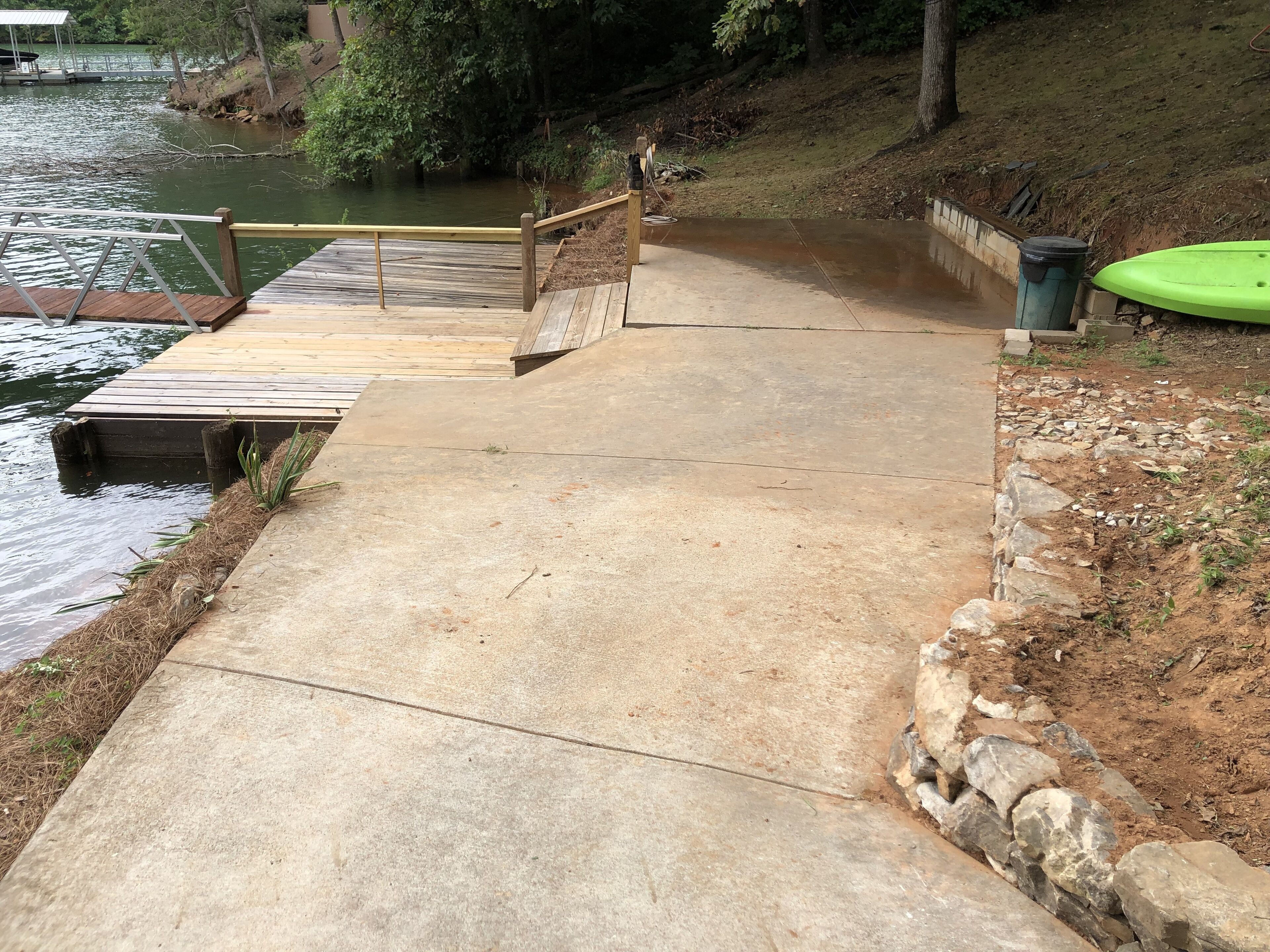A concrete pathway leading to a wooden dock over water, with a green kayak nearby.