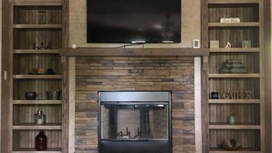Un salon doté d’une cheminée en pierre, d’un téléviseur à écran plat fixé au-dessus et d’étagères en bois de part et d’autre.