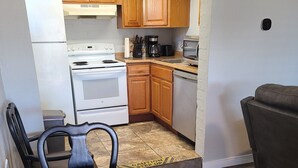 A compact kitchen with wooden cabinets, a white stove, and a dining area with a table and chairs.