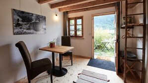 A cozy room with a wooden table, a chair, a potted plant, and a view of the outdoors through a window.