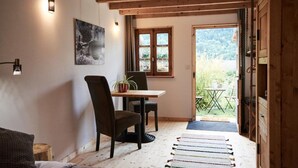 A cozy room with a wooden ceiling, a dining table with chairs, a potted plant, and a view of a garden through a window.