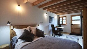 A bedroom with a wooden headboard, a bed with pillows, bedside lamps, a small table with chairs, and a window with curtains.
