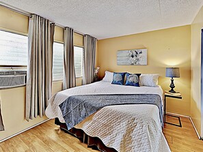A hotel room with a large bed, a bedside table with a lamp, and a window with curtains.