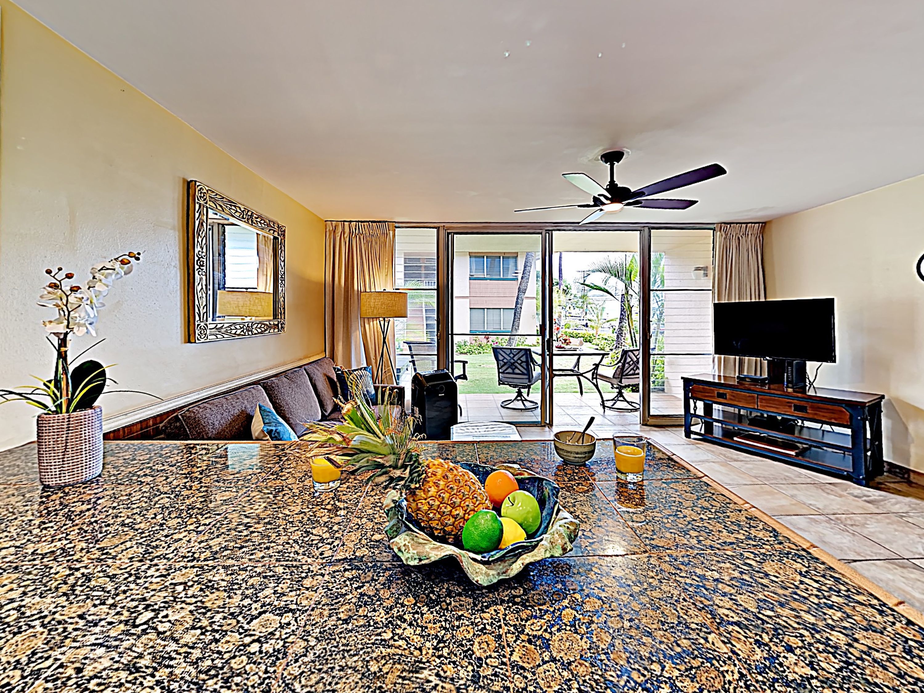 A living room with a sofa, a coffee table with fruit and drinks, a television, and a view of the outdoors.