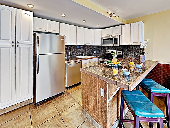 A modern kitchen with white cabinets, stainless steel appliances, a granite countertop, and a small island with stools.