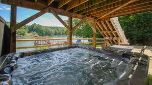 A hot tub under a wooden deck with a view of a lake and trees. - Big Splash-Lakefront Retreat with Hot Tub & Dock (Sherrills Ford)