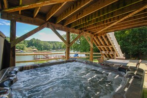 Un jacuzzi bajo una terraza de madera con vistas a un lago y árboles.