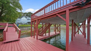 A red wooden dock with a covered walkway and stairs leading to a house. - Big Splash-Lakefront Retreat with Hot Tub & Dock (Sherrills Ford)