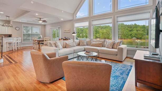 A spacious living room with a large L-shaped sectional sofa, a coffee table, and a dining area with a kitchen in the background. - Big Splash-Lakefront Retreat with Hot Tub & Dock (Sherrills Ford)