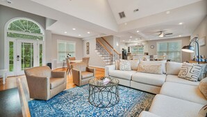 A spacious living area with a large sofa, armchairs, a coffee table, and a staircase leading to an upper level. - Big Splash-Lakefront Retreat with Hot Tub & Dock (Sherrills Ford)