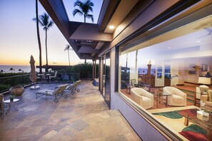A modern outdoor patio with a view of the ocean, furnished with lounge chairs and a dining area. - Mauna Kea Villas #13 w/AC: Luxurious Oceanview, Serene Lanai & Coastal Views (Kamuela)