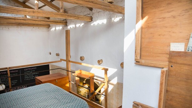 Een rustieke kamer met zichtbare houten balken, een slaapplein, een houten trap en een schoolbordmenu.