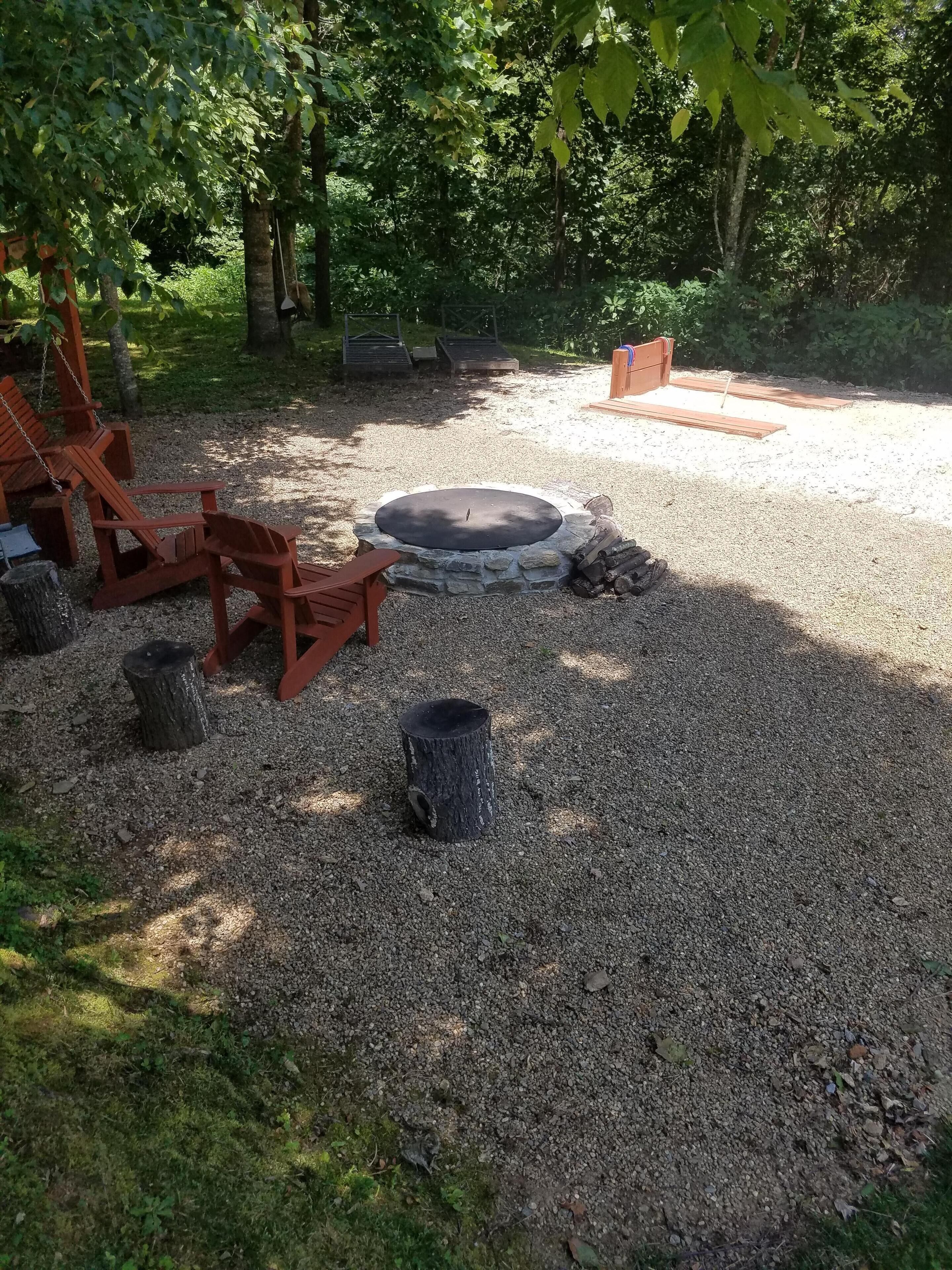 Een vuurkuil omringd door grind, met houten stoelen en een houten bank in de buurt.