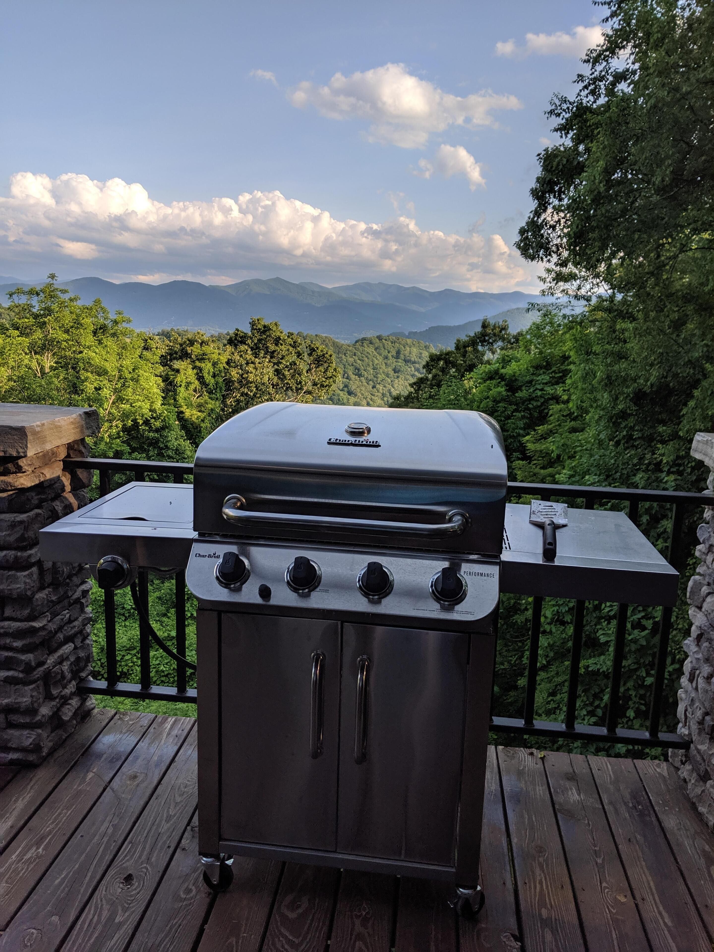 Un barbecue au charbon de bois sur une terrasse en bois, avec une vue panoramique sur les montagnes en arrière-plan.