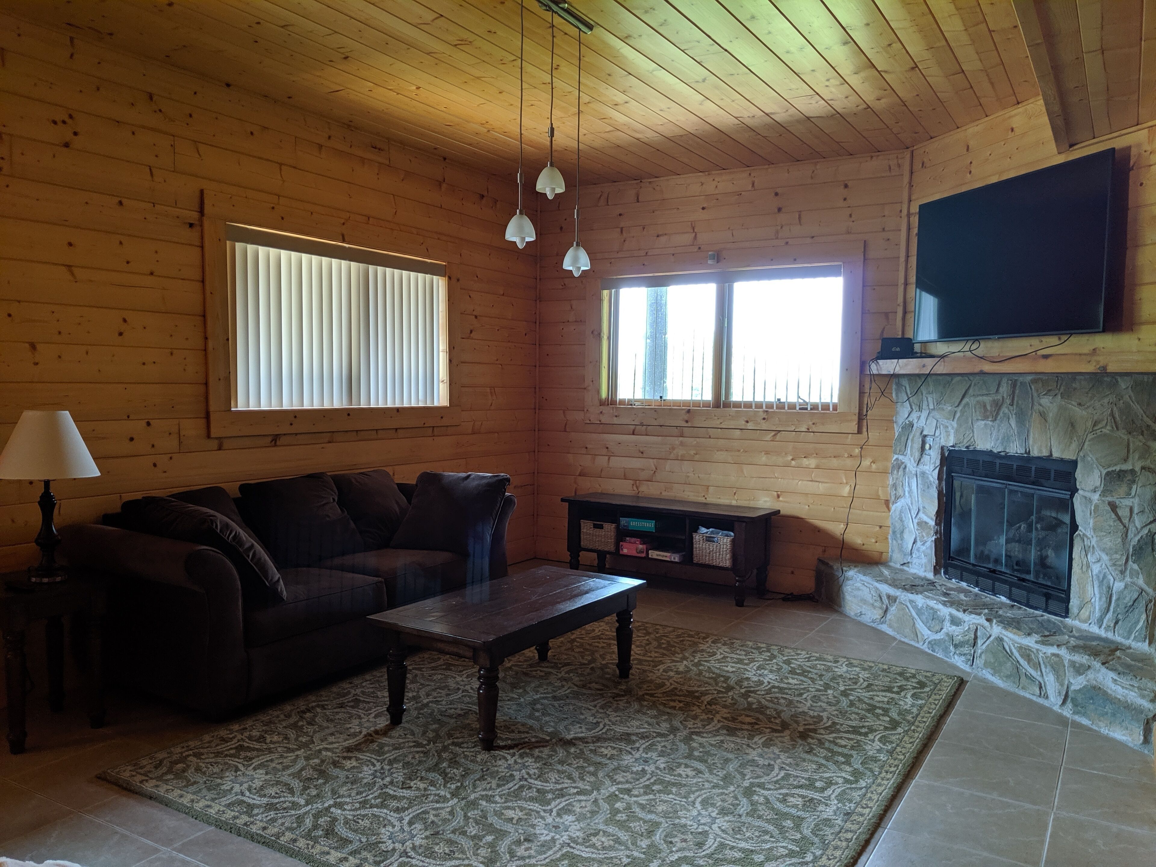L’intérieur chaleureux d’un chalet avec un plafond en bois, une cheminée en pierre, un canapé, une table basse et un téléviseur fixé au-dessus de la cheminée.