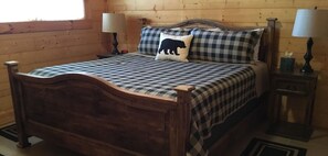 A wooden bed with a checkered bedspread and pillows, two bedside tables with lamps, and a wooden floor.