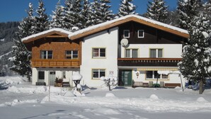 Ein zweistöckiges Gebäude mit einem hölzernen Balkon, einer Satellitenschüssel und einer verschneiten Landschaft.