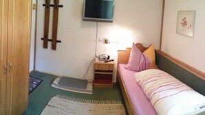 Ein Schlafzimmer mit einem Bett, einem Nachttisch, einem an der Wand montierten Fernseher, einem Holzschrank und einer Tür.