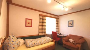 Ein kleines, gemütliches Zimmer mit einem Bett, einem Sofa, einem Tisch und zwei gerahmten Bildern an den Wänden.