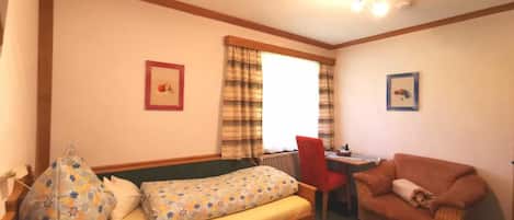 A small, cozy room with a bed, a sofa, a table, and two framed pictures on the walls.